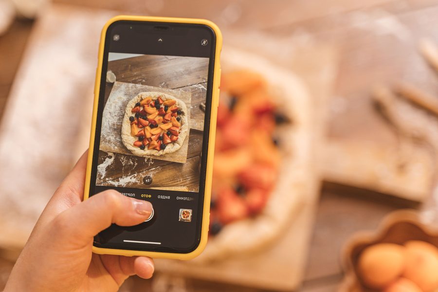 A phone photographing a fresh fruit galette on a wooden board