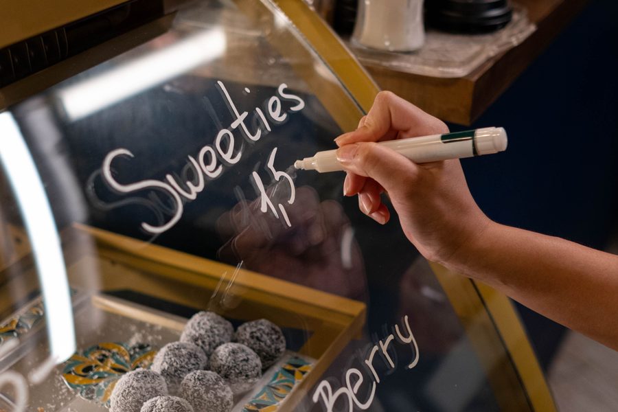 A hand writing prices on a bakery display case